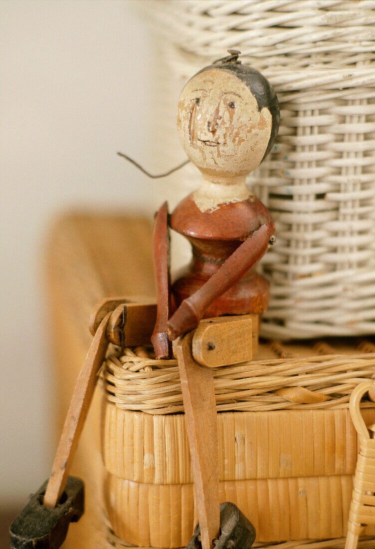 A detail of an antique wooden doll placed on a wicker hamper