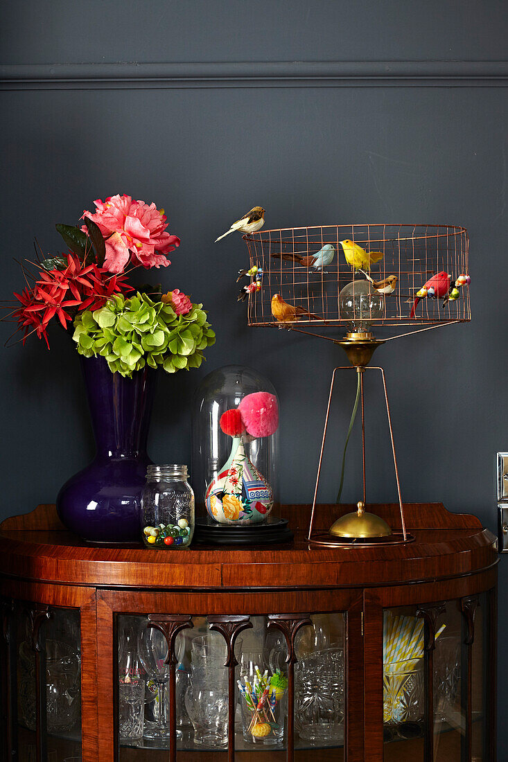 Artificial birds on vintage lamp with cut flowers on cabinet in Brighton home East Sussex, UK