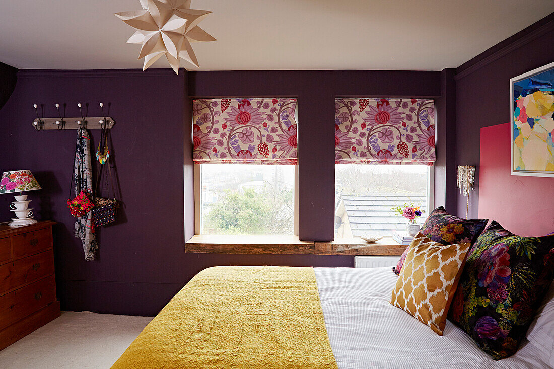 Geblümte Jalousien an Fenstern und große Dekokissen auf Bett in farbenfrohem Schlafzimmer in einem Haus in Brighton, East Sussex, UK