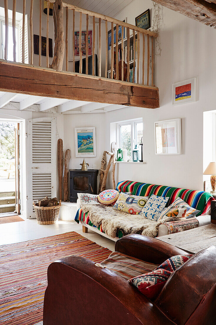 Striped sofa with cushions and vintage leather armchair in double height Bridport home, Dorset, UK