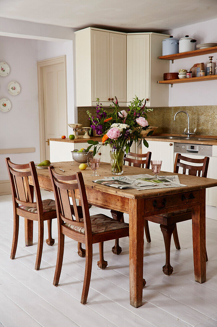 Schnittblumen und Zeitung auf Holztisch mit Stühlen in der Küche eines Hauses in Hampshire aus dem 17. Jahrhundert