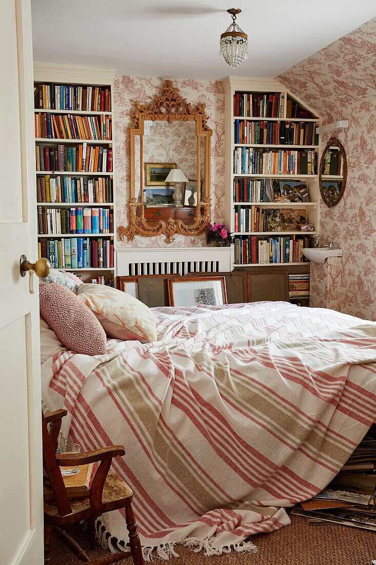Ungemachtes Bett, Bücherregale und Toile de Jouy-Tapete in einem Haus aus dem 17. Jahrhuundert in Hampshire, England, UK
