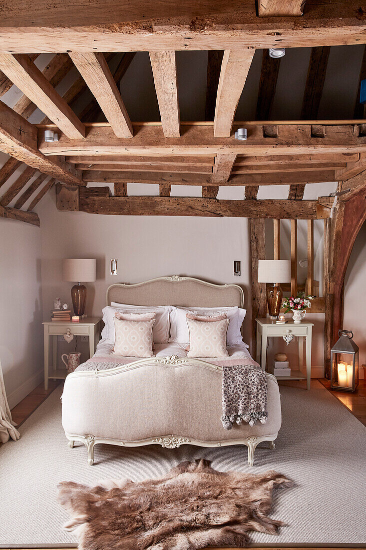 Antikes französisches Bett mit Lampen und Fellteppich in einem unter Denkmalschutz stehenden Bauernhaus mit Holzbalken (Grade II) in Kent, UK