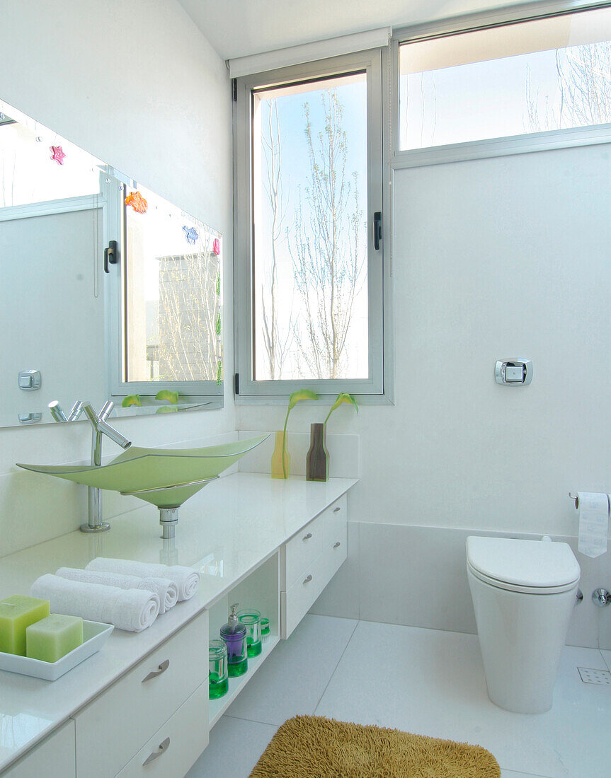 Modernes weißes Badezimmer mit großem Spiegel und Waschbecken aus farbigem Glas und Blick nach draußen