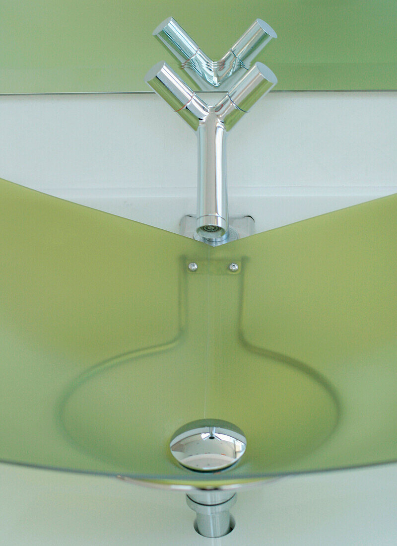 Detail eines Waschbeckens aus grünem Glas mit Stahlarmaturen