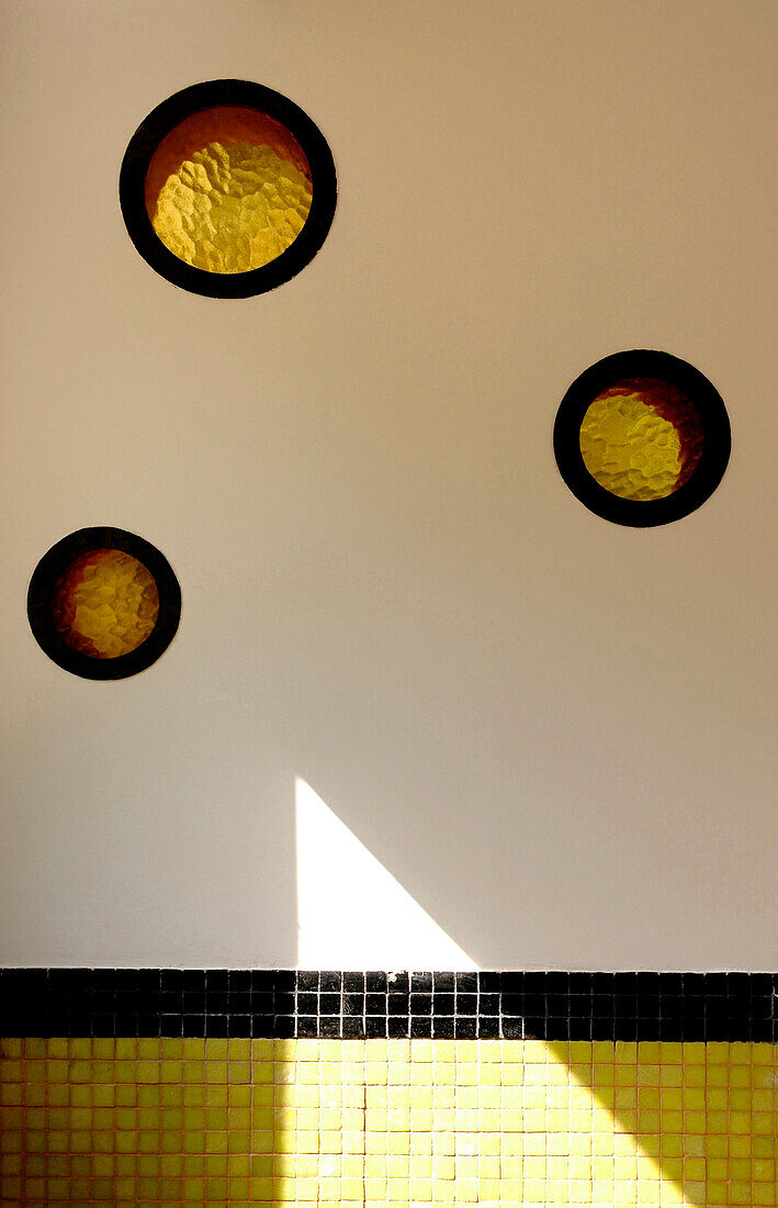 Geometrische Fliesen und kleine runde gelbe Fenster an der Wand