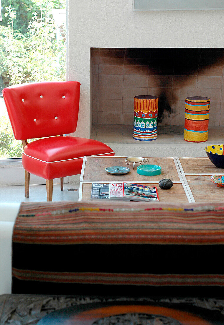Roter Stuhl aus den 1960er Jahren mit Couchtisch aus lackiertem Holz neben einem Kamin aus Beton
