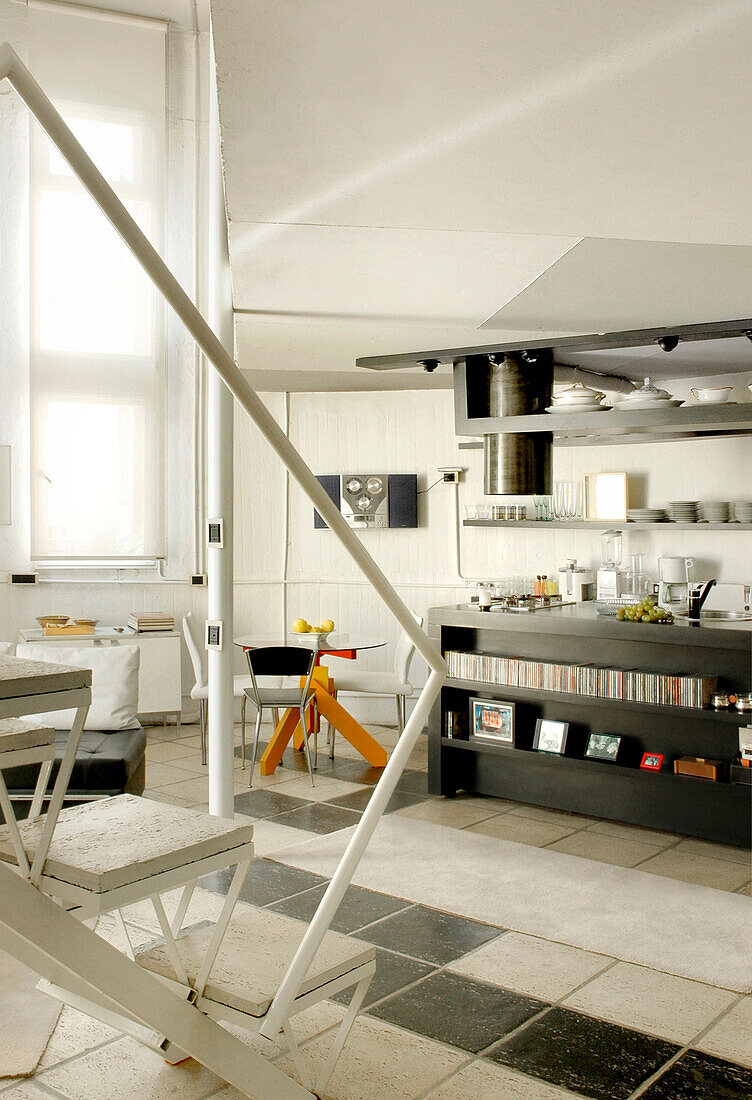 Offener Küchenbereich mit Ofenrohr aus emailliertem Eisen über einer Arbeitsfläche aus schwarzen Laminatplatten davor Teppich aus Naturwolle