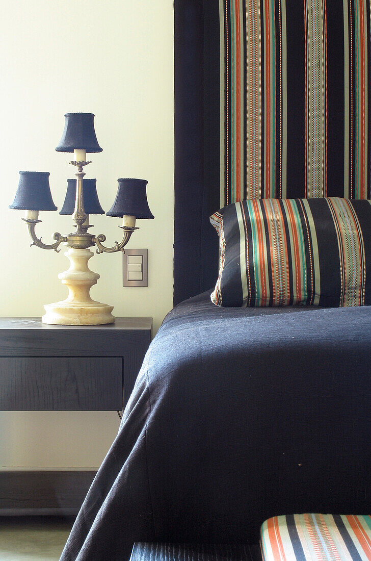 Schlafzimmer mit schwarzen Holzmöbeln, bunten handgewebten Stoffen, einer Baumwoll-Bettdecke und einer antiken Lampe