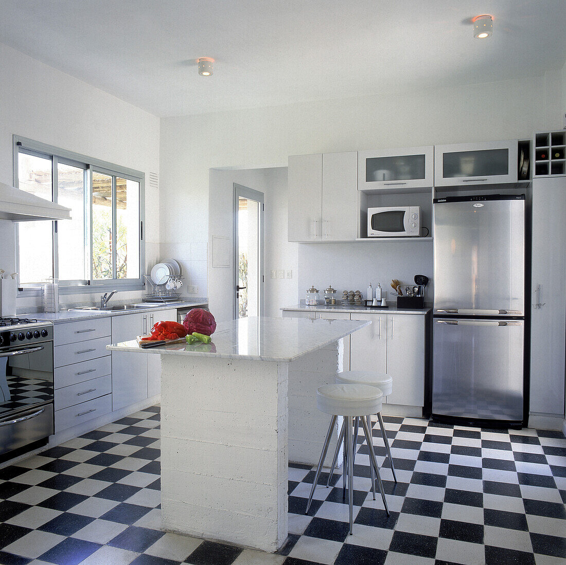 Küche im Schachbrettmuster mit Melaminmöbeln, Stahlbeschlägen und einer Kücheninsel aus Beton mit einer Platte aus Carrara-Marmor