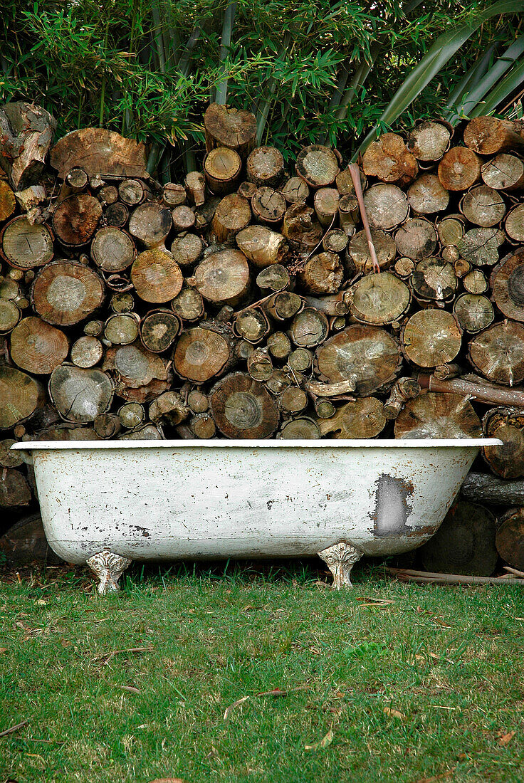 Vintage-Badewanne im Garten vor Stapel mit Brennholz