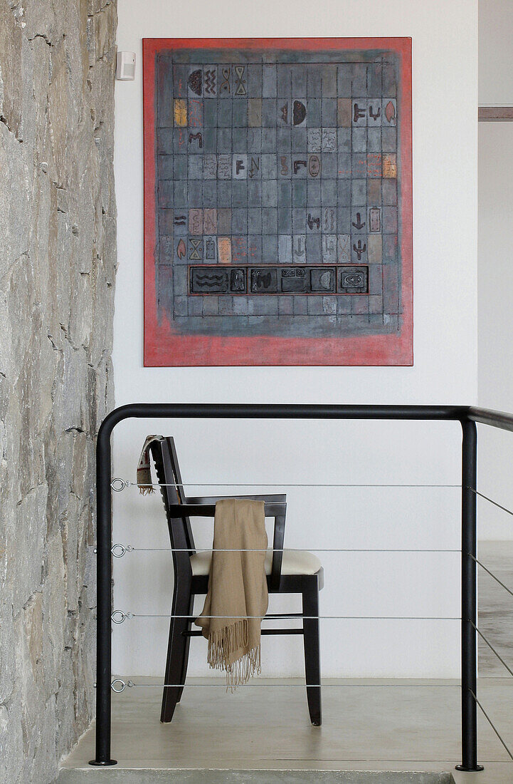 Polsterstuhl unter abstraktem Kunstwerk im Flur mit Geländer und freiliegender Steinwand