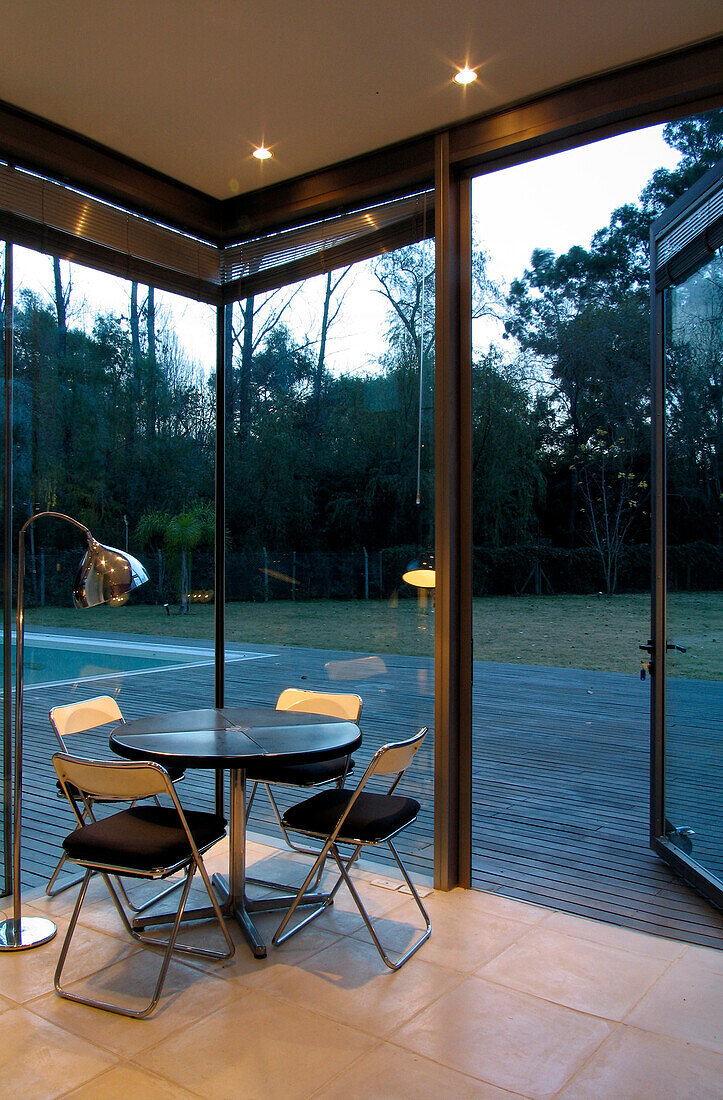 Tisch und Stühle in einer Zimmerecke mit Blick durch eine offene Glastür auf eine Veranda