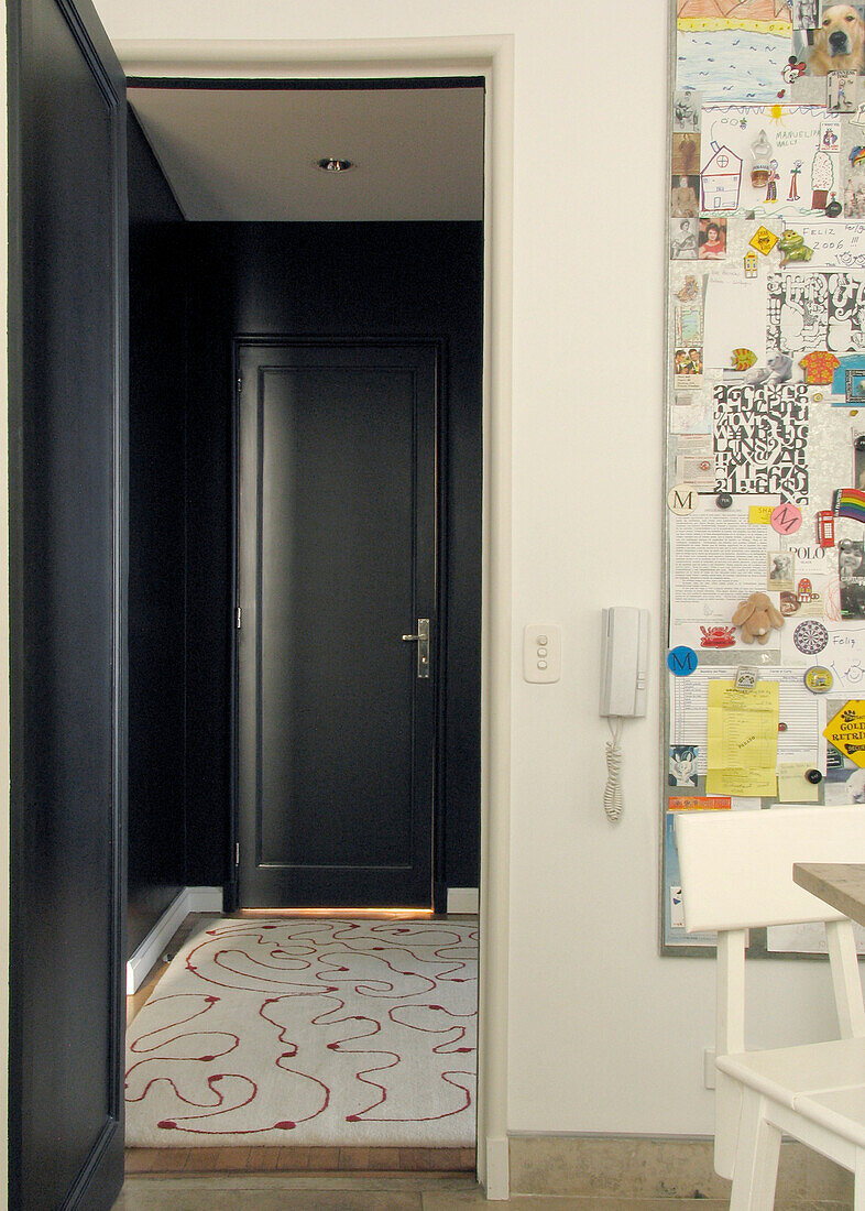 Kitchen noticeboard with view through doorway to black painted hallway with patterned rug