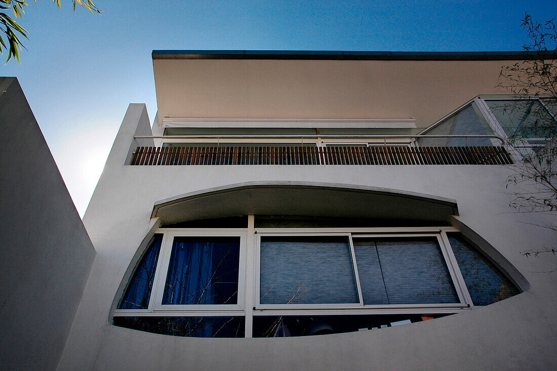 Moderne Stuckfassade mit weißem Aluminiumbalkon und Fenster in Augenform