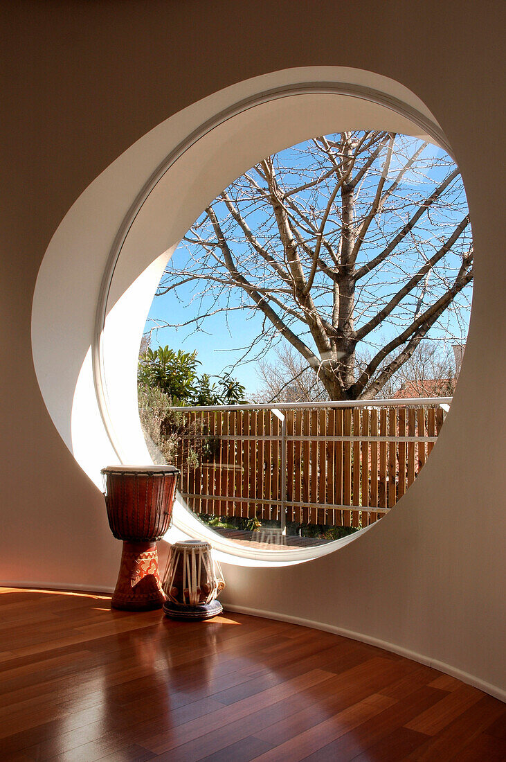 Trommeln am großen runden Fenster in einem Raum mit rotem Eukalyptusboden