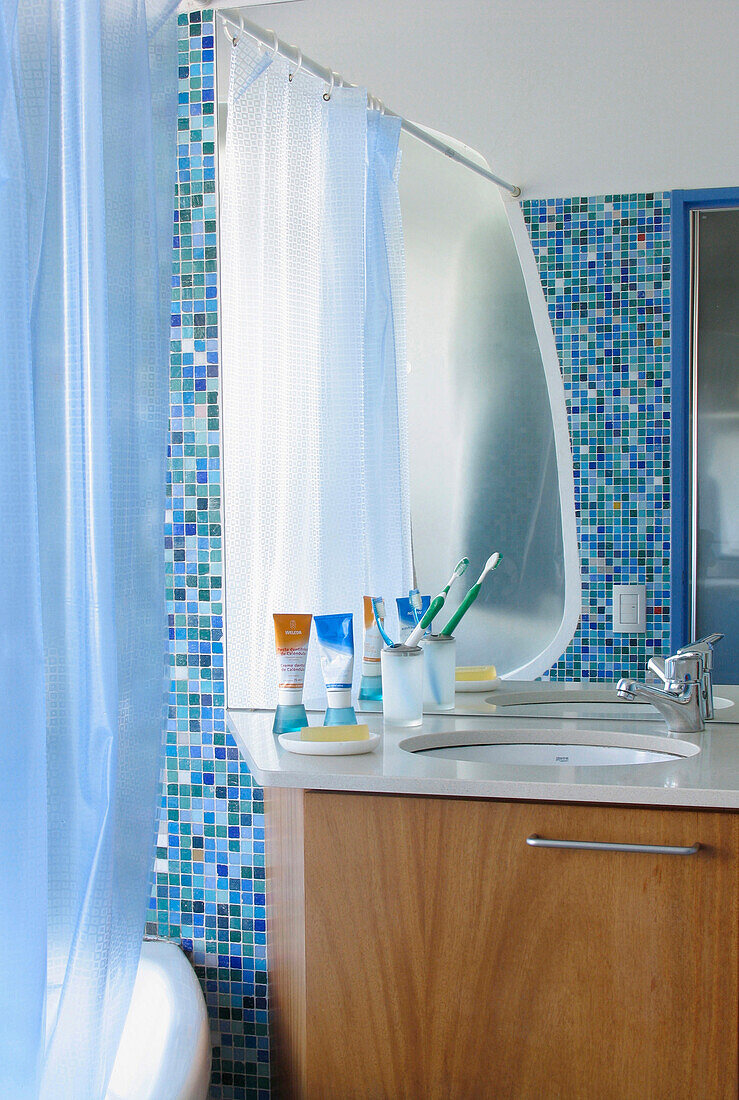 Toiletries on washbasin in tiled bathroom with shower curtain