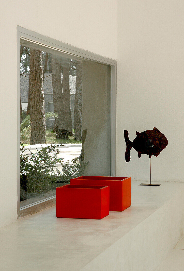 Zwei rote Kästen und eine Fischskulptur vor Wohnzimmerfenster mit Blick auf den Waldgarten