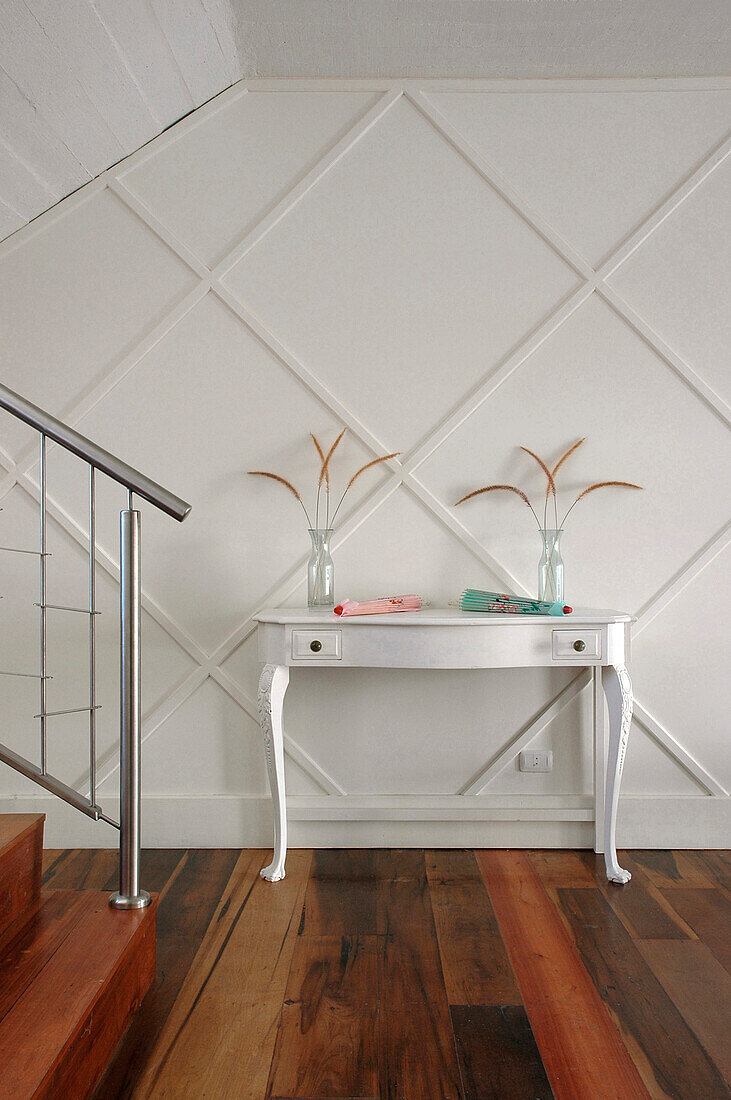 White painted console table in panelled hallway with stainless steel banister