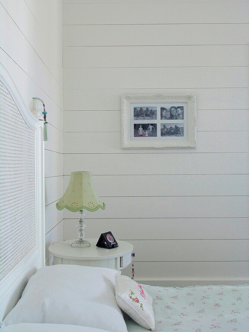 Nachttisch mit Lampe in einem weiß gestrichenen Zimmer mit gerahmten Fotografien