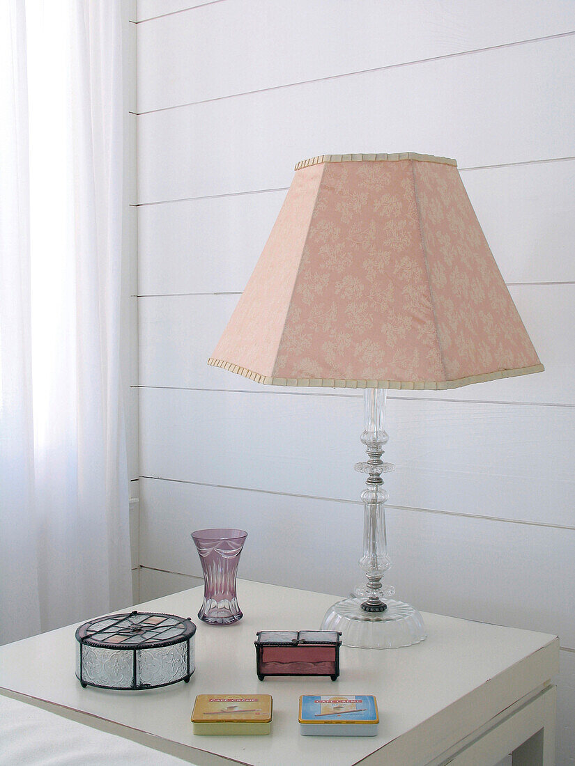 Lampe mit rosafarbenem Schirm und Schmuckkästchen auf einem Tisch