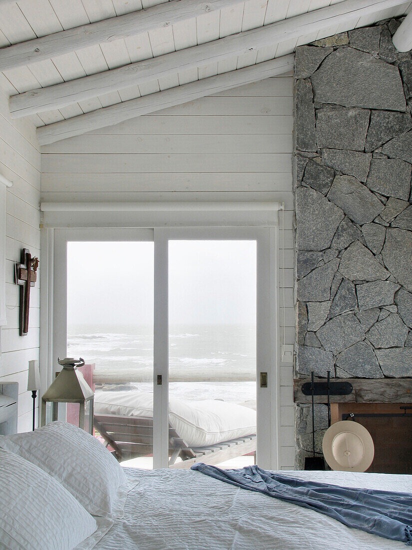 Bedroom with panelled ceiling and exposed stone wall door opening to coastal terrace