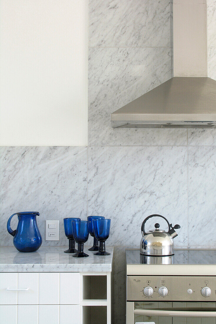 Blue glassware and kettle on hob in Carrara marble kitchen