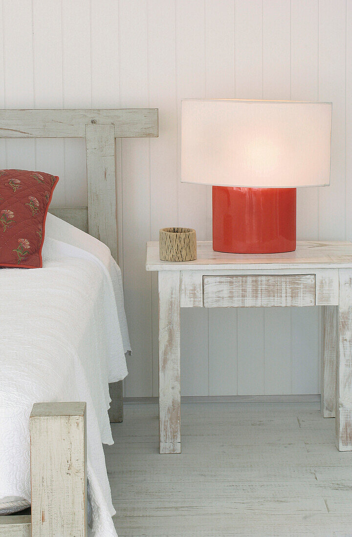 White pique bedspread with red Kilim cushions and red ceramic lamp
