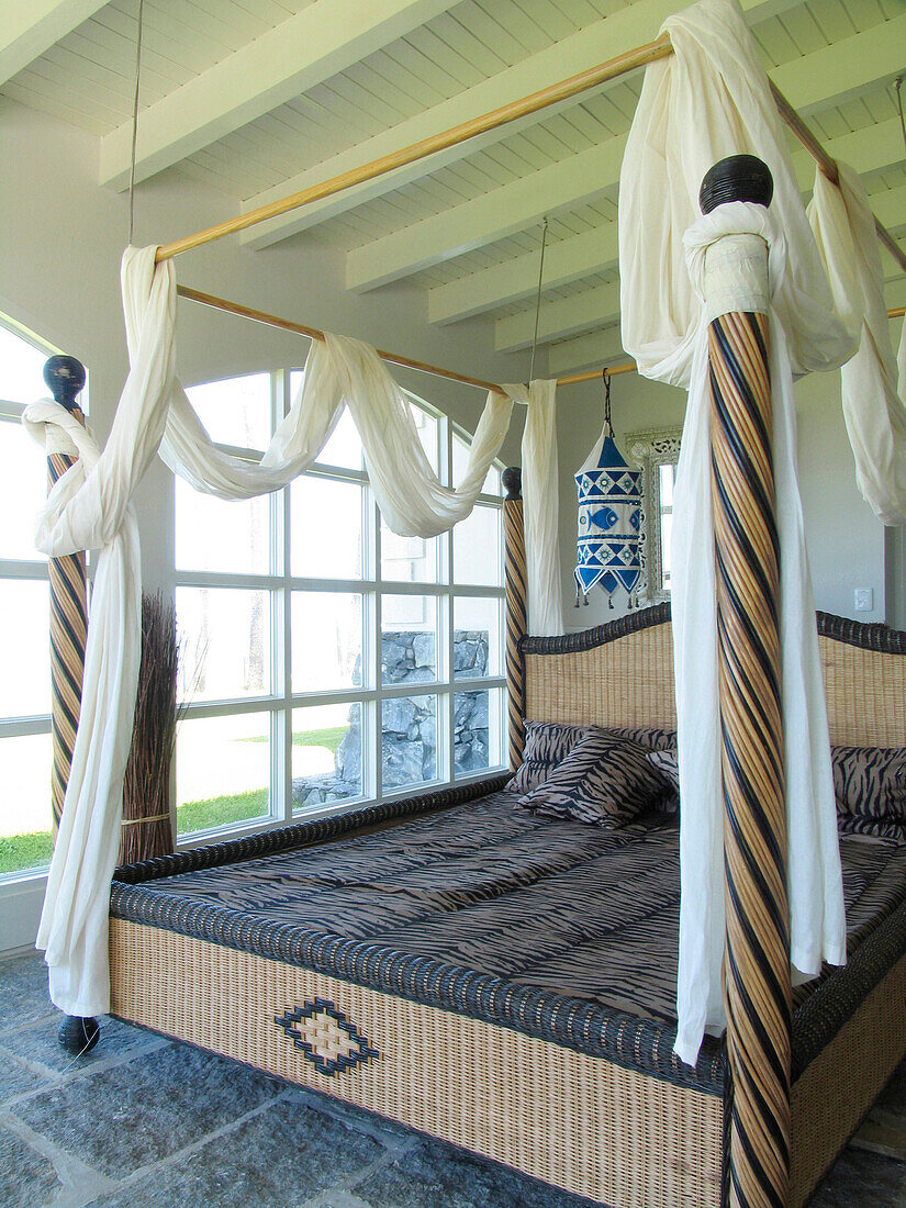 Four poster bed with swathes of fabric in beamed room with large windows
