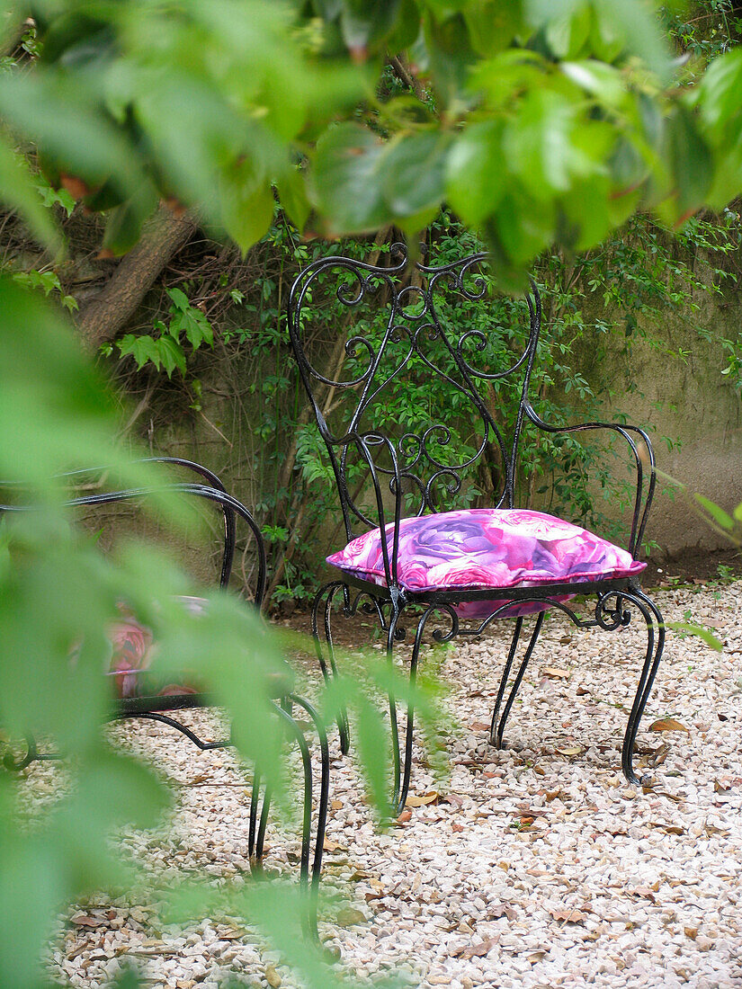 Schmiedeeiserner Stuhl mit rosa Blumenmuster auf einer Kiesterrasse