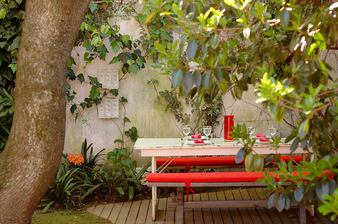 Sitzbank mit roten Kissen im Innenhof eines ummauerten Gartens