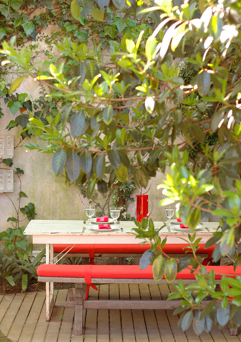 Sitzbank mit roten Kissen im Innenhof eines ummauerten Gartens