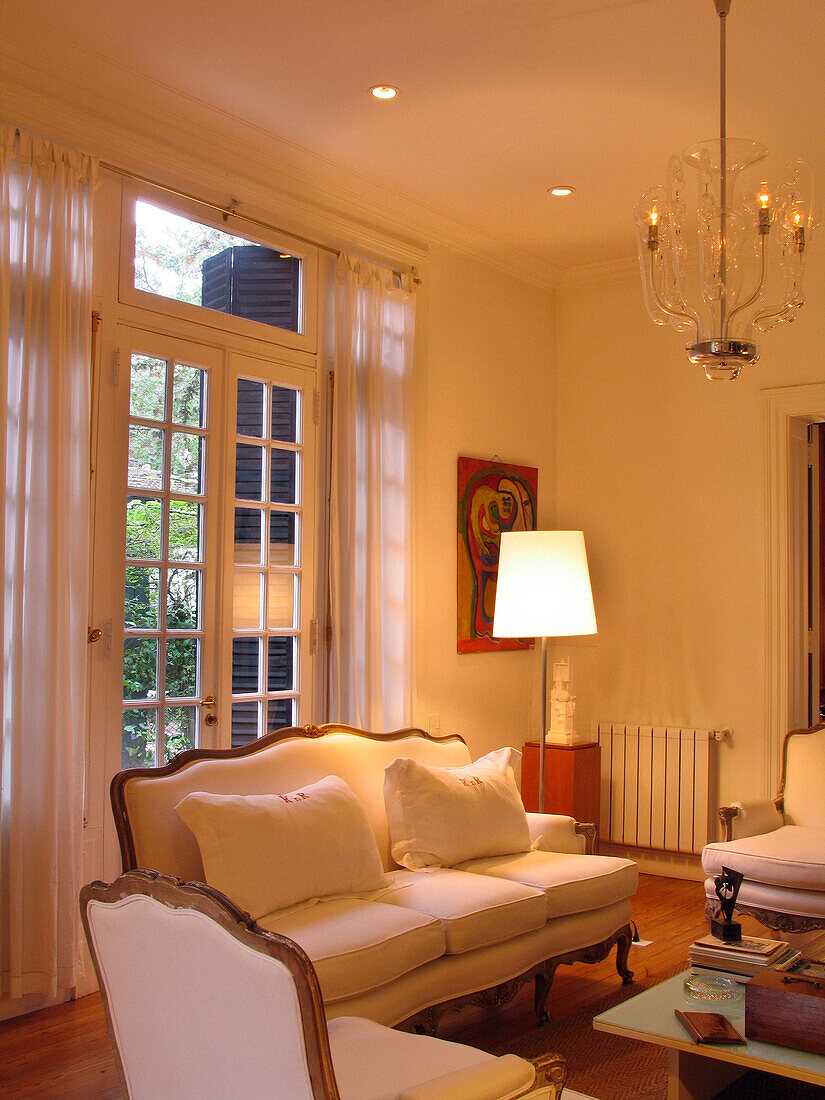 Weiße dreiteilige Sitzgarnitur in einem beleuchteten Raum mit Vorhängen und Terrassentüren
