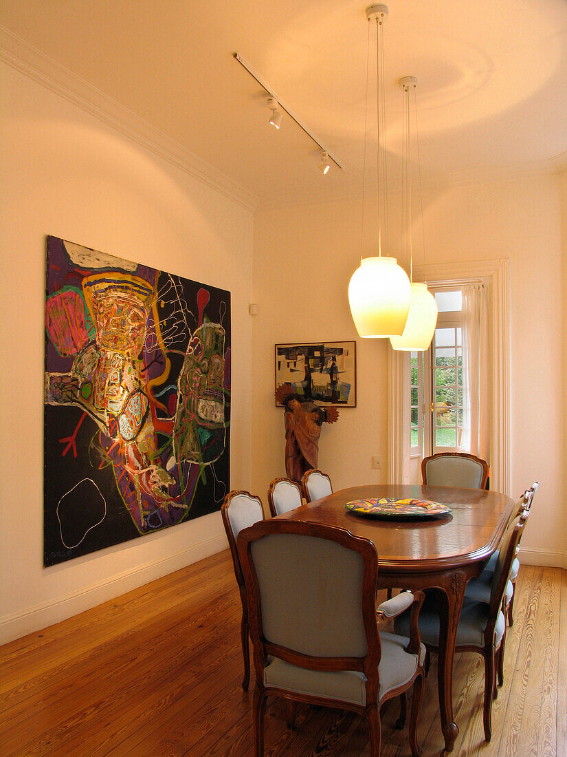 Lit pendant lights over wooden dining room table with art work from Brazil