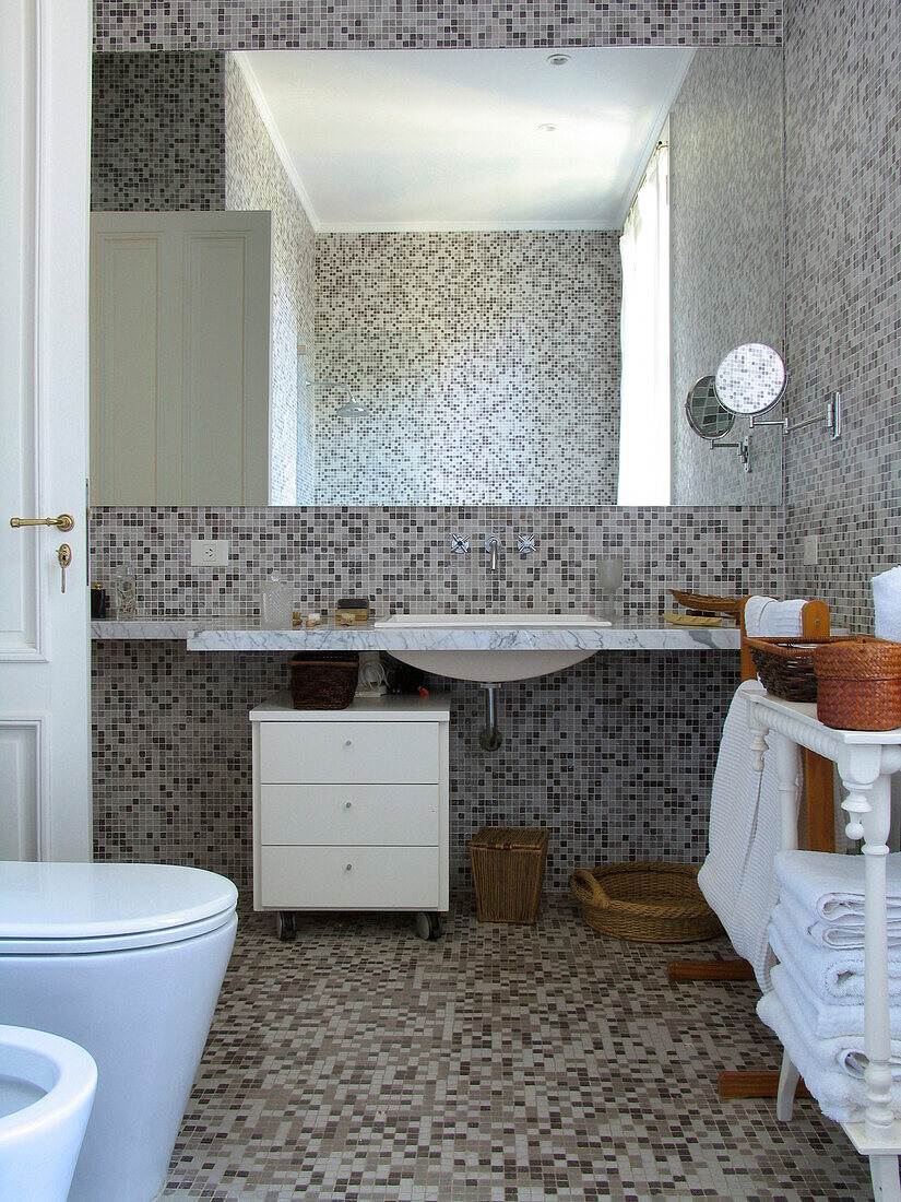 Large mirror above wash basin in grey tiled bathroom with under sink storage drawers