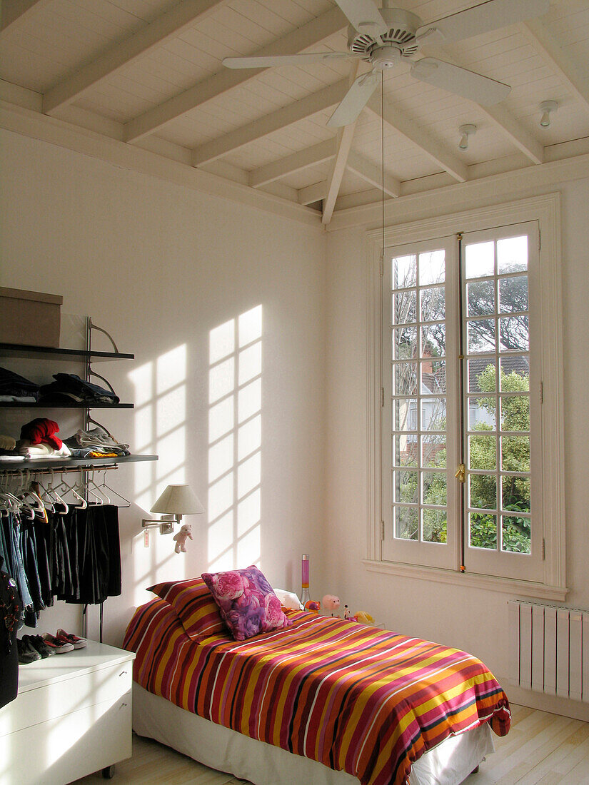 Gestreifter Bettbezug auf einem Einzelbett in einem Kinderzimmer mit hoher Decke und Ventilator
