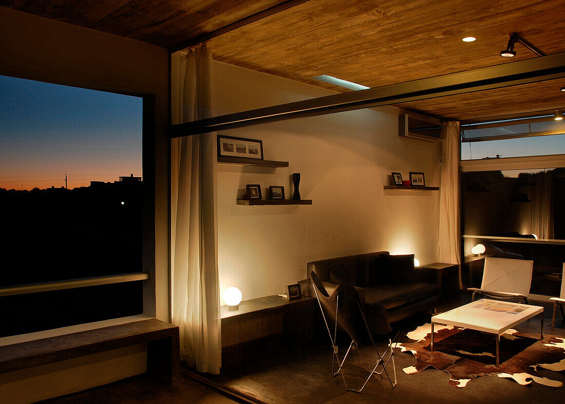 Sitzecke mit Couchtisch in einem beleuchteten Wohnzimmer mit Trennvorhängen und holzgetäfelter Decke