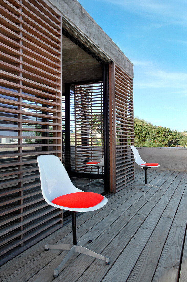 Deck aus behandeltem Kiefernholz mit Jacobsen-Stühlen mit roten Sitzen und Lapacho-Holzschirm