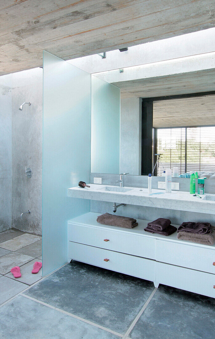 Bathroom with screened Carrara marble sinks and embedded mirror under skylight shower floor with pre-cast concrete tiles which allow water to drain