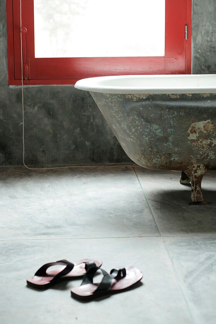 Bathroom with stucco walls coloured with Portland cement antique tub and a pair of sandals