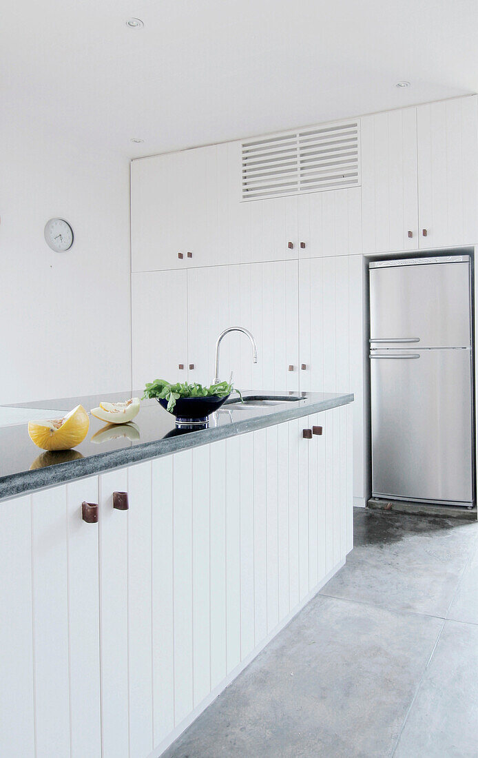 Salatzubereitung auf weiß getäfelten Schränken in einer Küche mit silbernem Kühlschrank