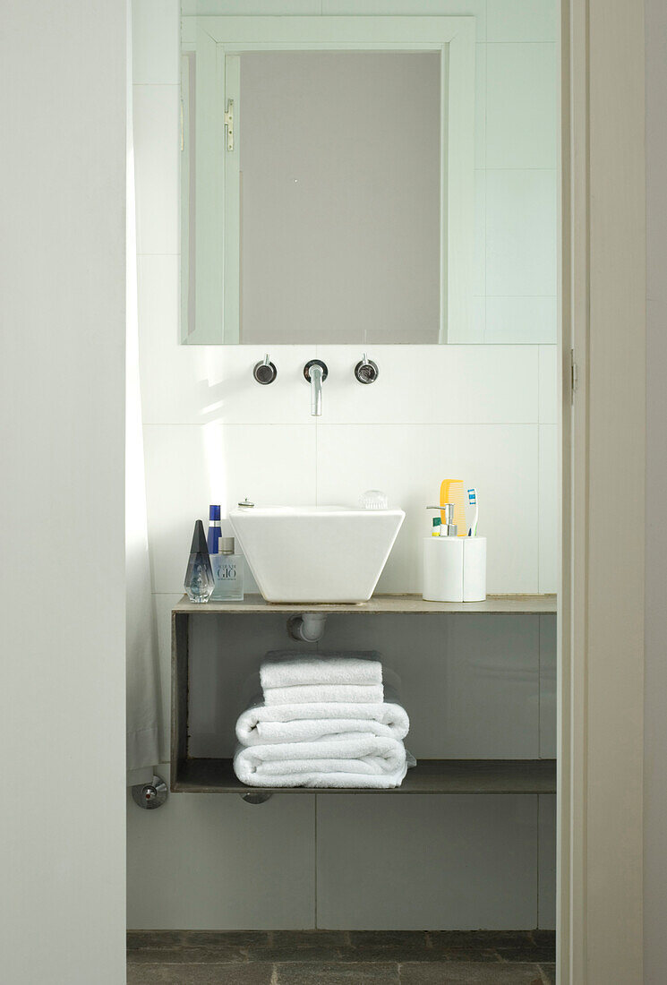 Wall mounted mixer taps above washbasin and folded towels on shelf