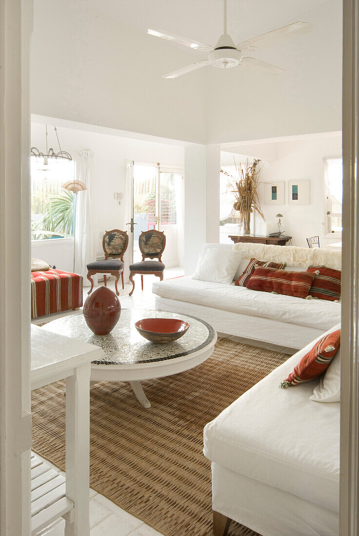 Ganz in Weiß gehaltenes Wohnzimmer mit Terrakotta- und grünen Details und einem L-förmigen Sofa