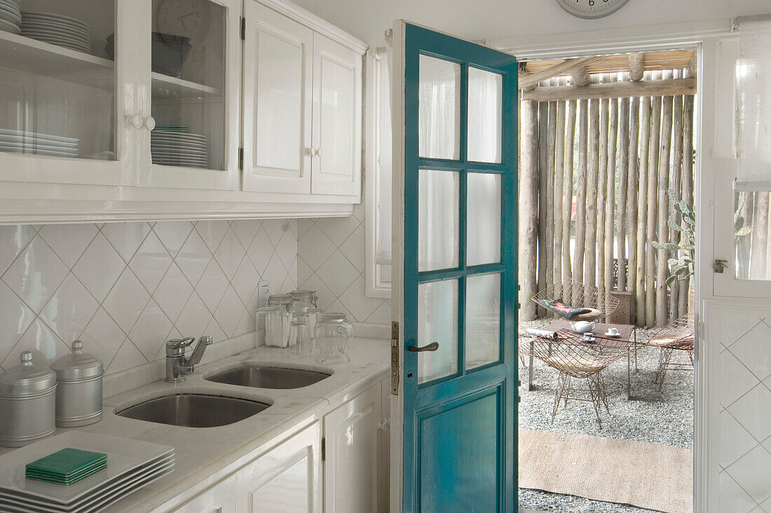 Küche mit türkisfarbener Tür und Blick auf die Außenterrasse mit Kiefernholzzaun