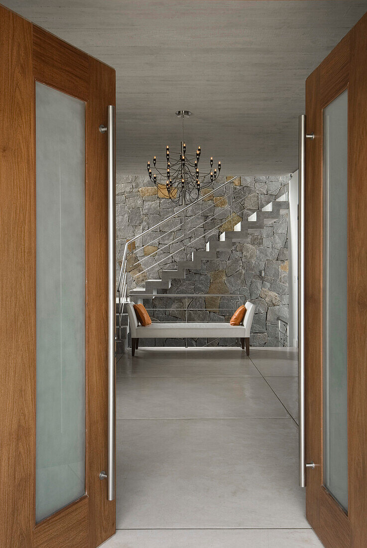 View through double doors to entrance with staircase set against exposed stone wall