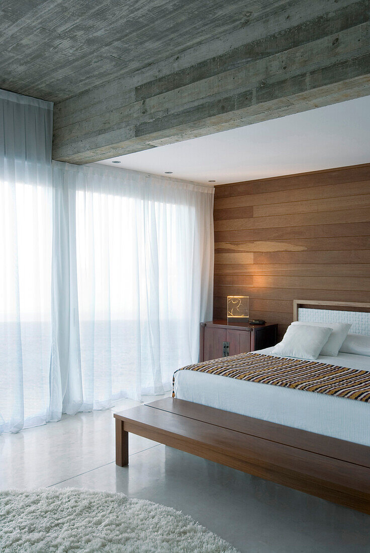 Panelled bedroom with concrete ceiling and closed net curtains