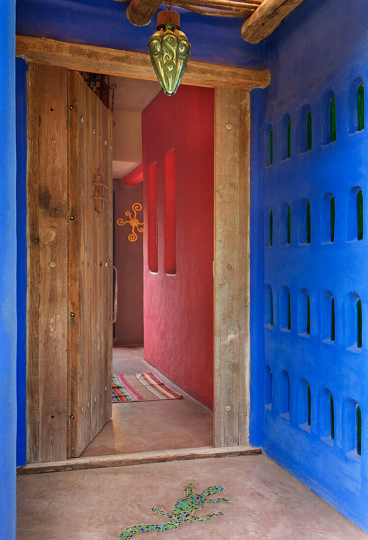 Offene Haustür mit kontrastierenden Wänden mit Flaschenverkrustung und Betonboden mit Leguan aus grünen venezianischen Fliesen