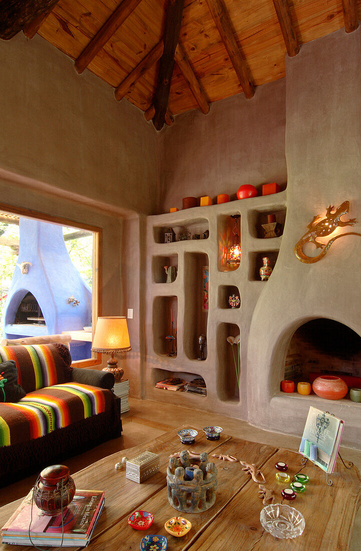 Wohnzimmertisch mit Ornamenten auf Eichenbrettern und Nischenregal aus Beton mit Kamin, der an einen alten Lehmofen erinnert