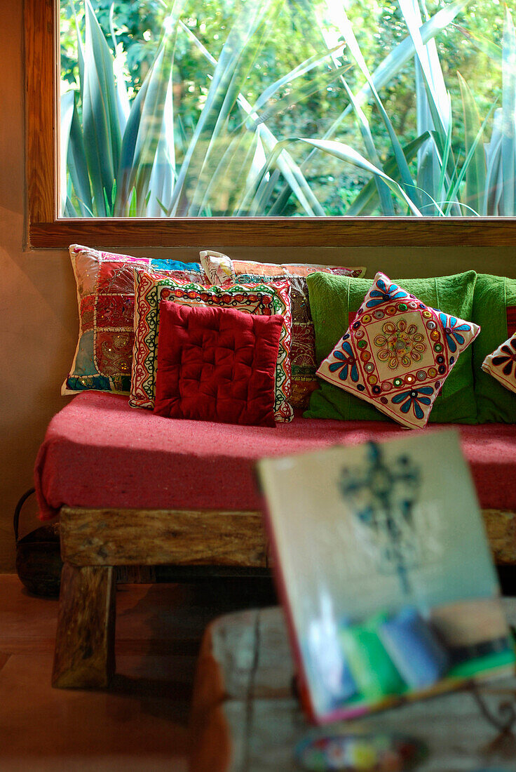 Sofa aus wiederverwendetem Eichenholz mit Kissen in verschiedenen Farben und Texturen am Fenster mit Kaktus