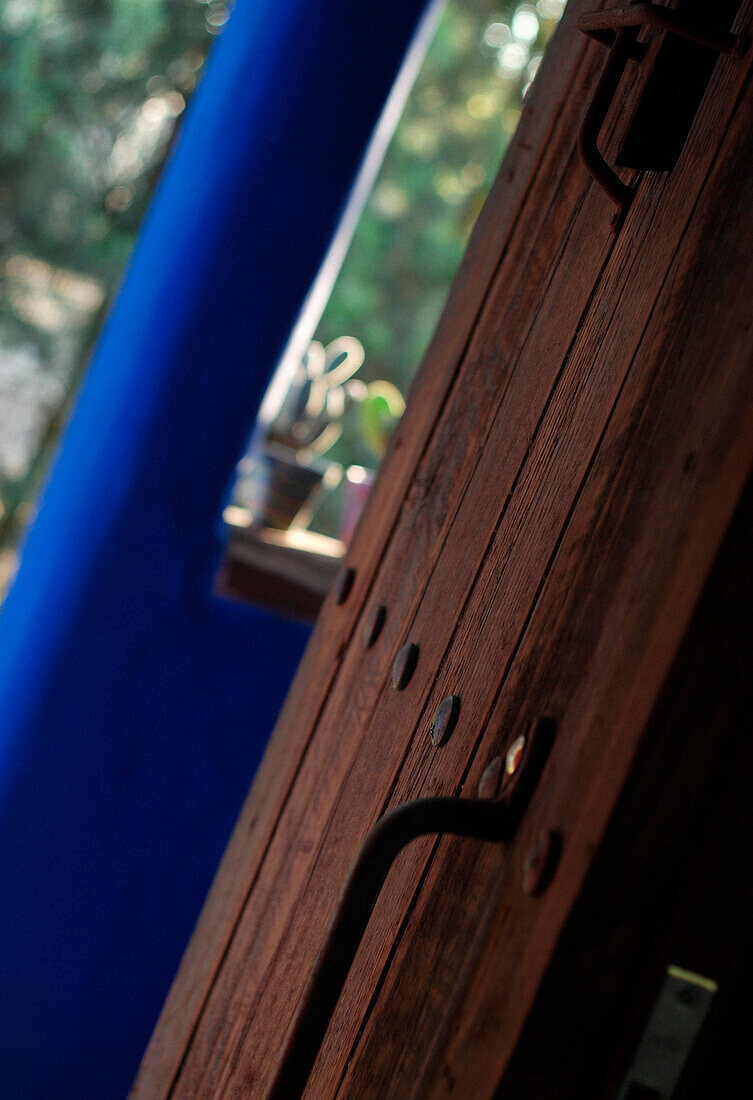 Wooden door with iron handle and studwork set against blue painted exterior porchway
